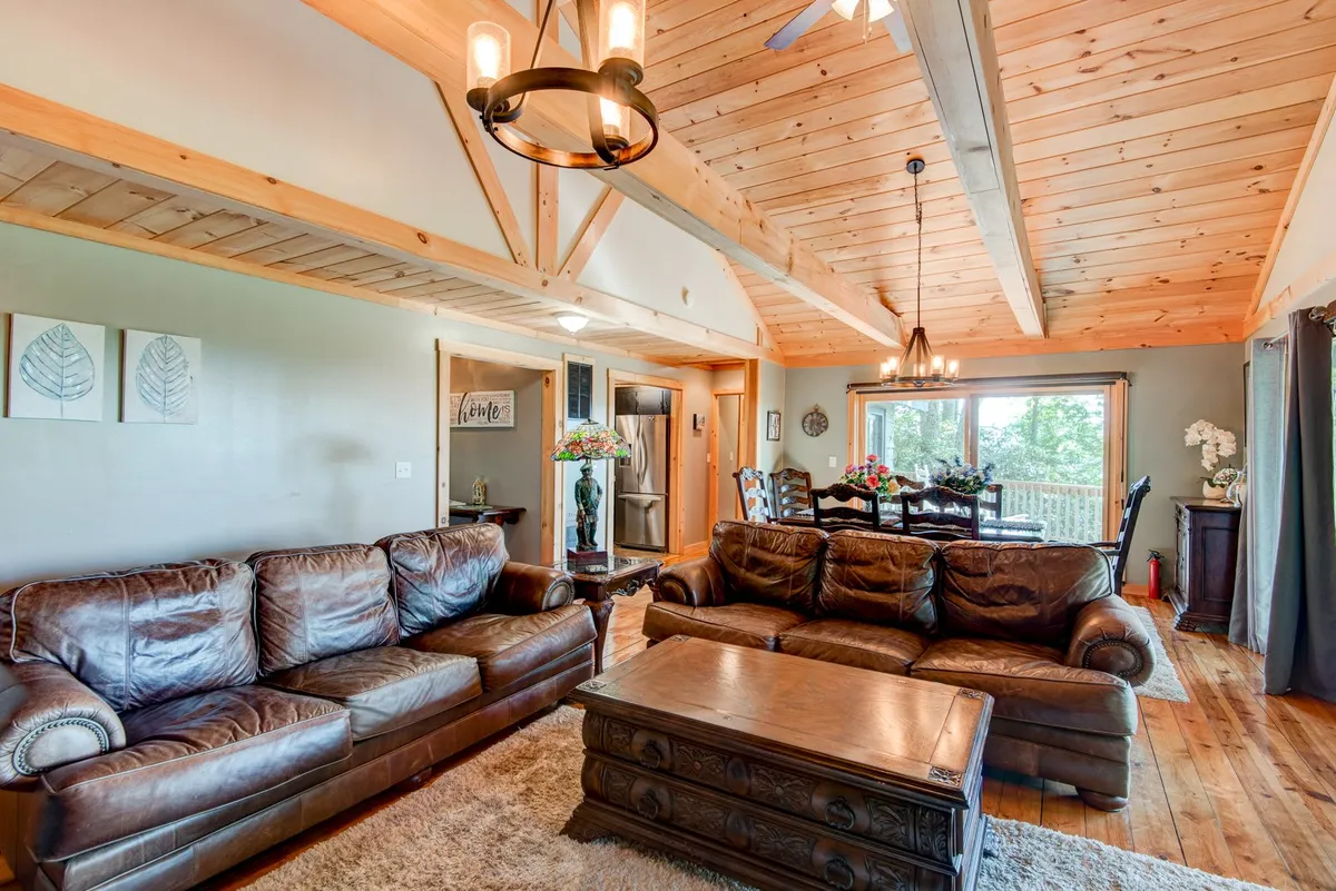 A view of the great room and dining area in a seamless open-concept layout. Leather sofas and a wooden coffee table create a relaxing lounge area, while a dining table is visible in the background, all set against large windows that flood the space with mountain light.