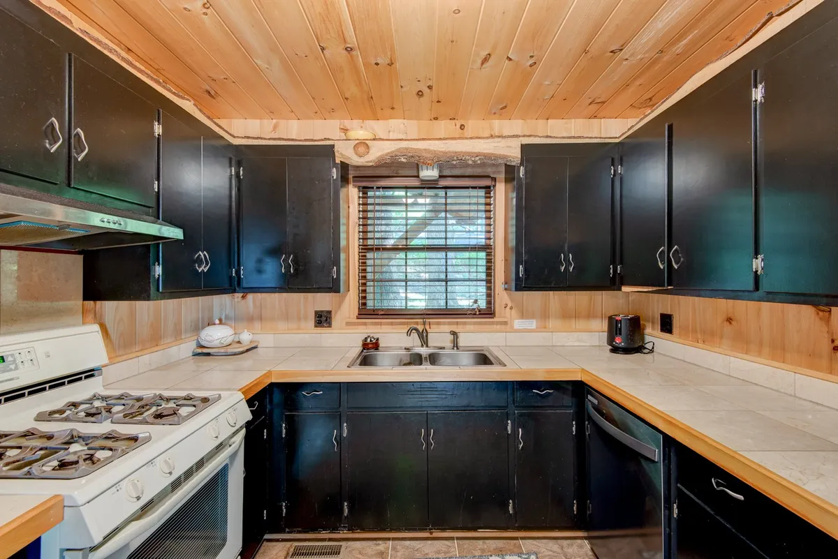 A close-up view of the kitchen workspace, with black cabinets, a wooden ceiling, a kitchen sink, and a stove as the focal points—demonstrating a functional and stylish cooking area. The setup emphasizes readiness for meal preparation and gathering.
