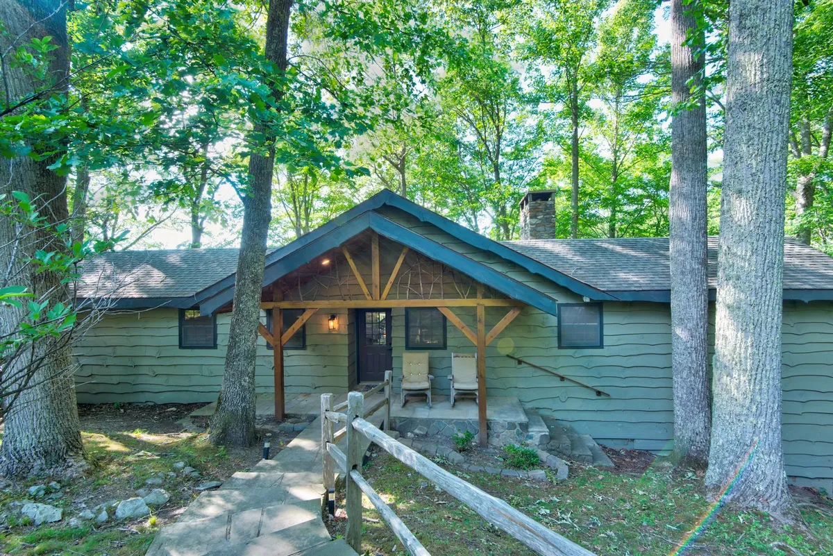 A cozy wooden porch with a stone pathway winding through large trees, inviting guests to relax, enjoy nature walks, or gather around a fire pit. The scene highlights both the porch and easy access to natural trails.