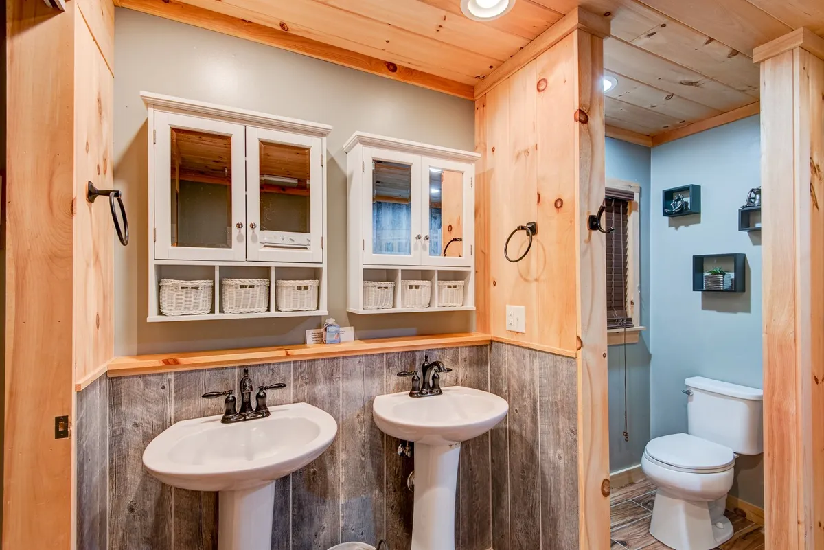This image features a bright bathroom with dual pedestal sinks, elegant wooden cabinetry, wall-mounted mirror cabinets, and subtle wood paneling. The space is designed for both function and relaxation, evoking a spa-like feel ideal for refreshing routines.