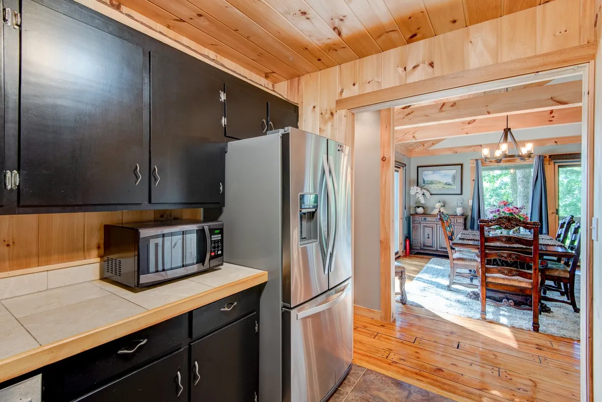 A kitchen featuring a stainless steel refrigerator, black cabinetry, a wooden countertop, and an open archway that leads into the dining area, blending culinary and social spaces. The layout fosters connection between the cook and guests or family in adjacent rooms.