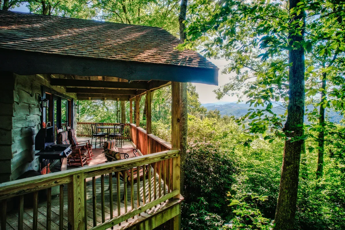 A tranquil porch scene featuring classic wooden rocking chairs looking out over an expansive view of rolling mountains and lush greenery. The soft light suggests either morning or dusk, setting a romantic and peaceful ambiance. The setting is perfect for enjoying a quiet cup of coffee or a glass of wine while taking in the breathtaking mountain vistas.